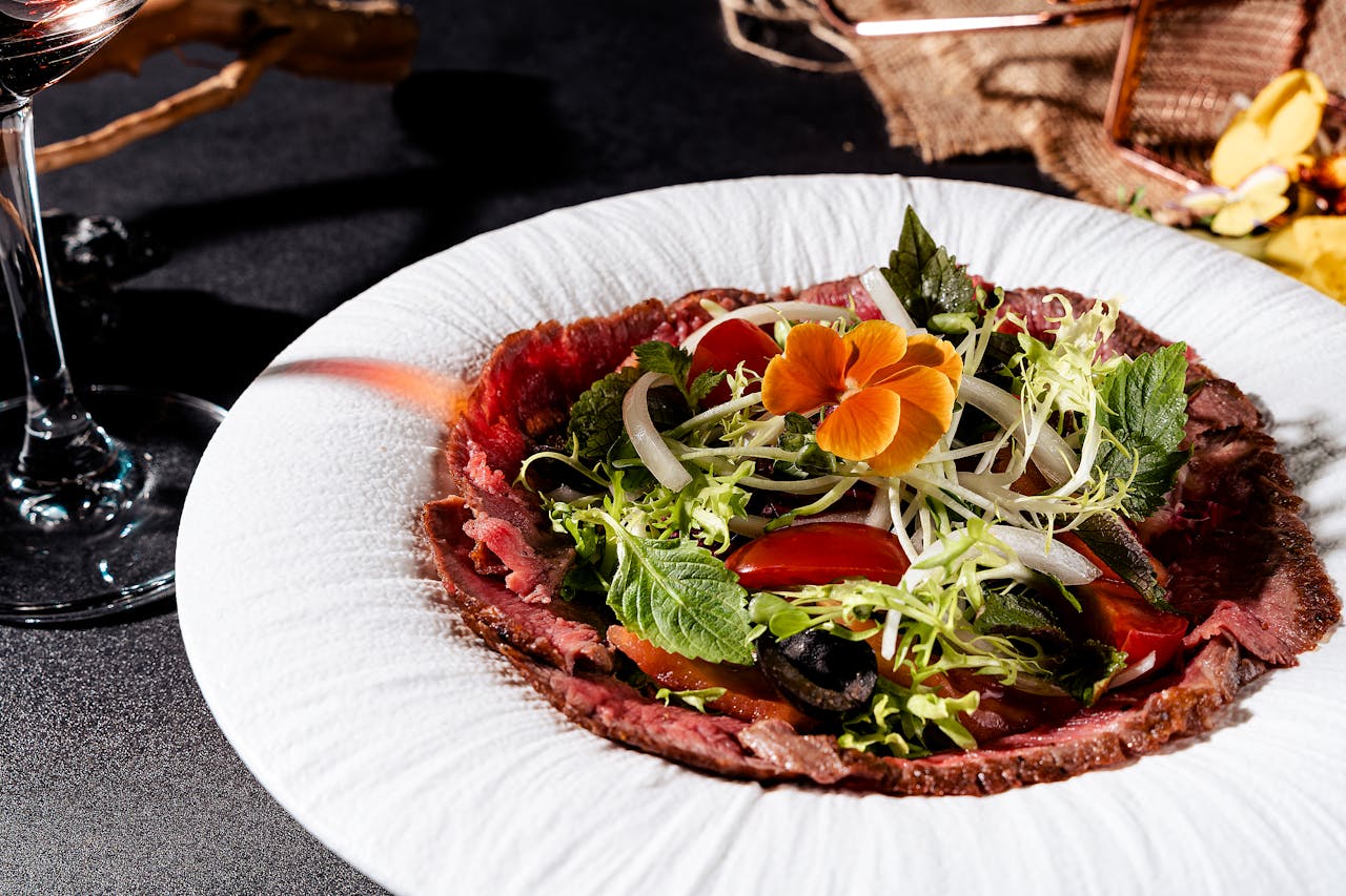 A fresh and vibrant gourmet beef carpaccio dish with leafy greens and edible flower garnish.